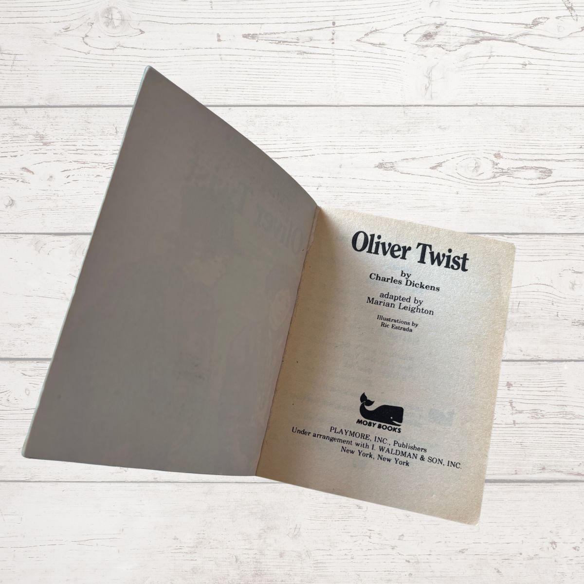 Open book titled 'Oliver Twist' by Charles Dickens on a light wooden surface