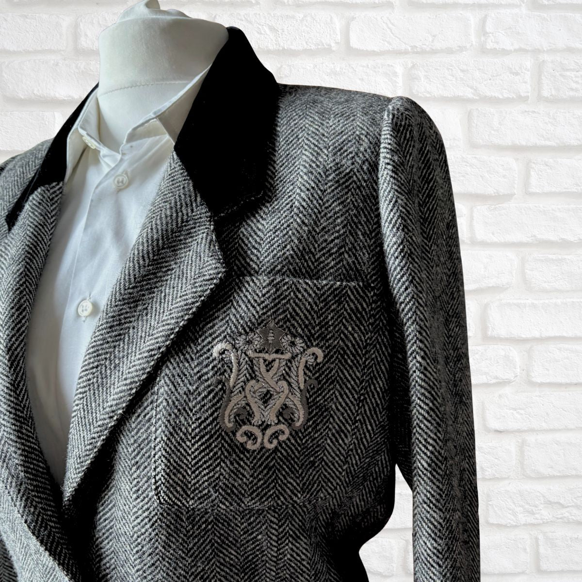 herringbone blazer with a prominent emblem on a mannequin against a white brick wall.