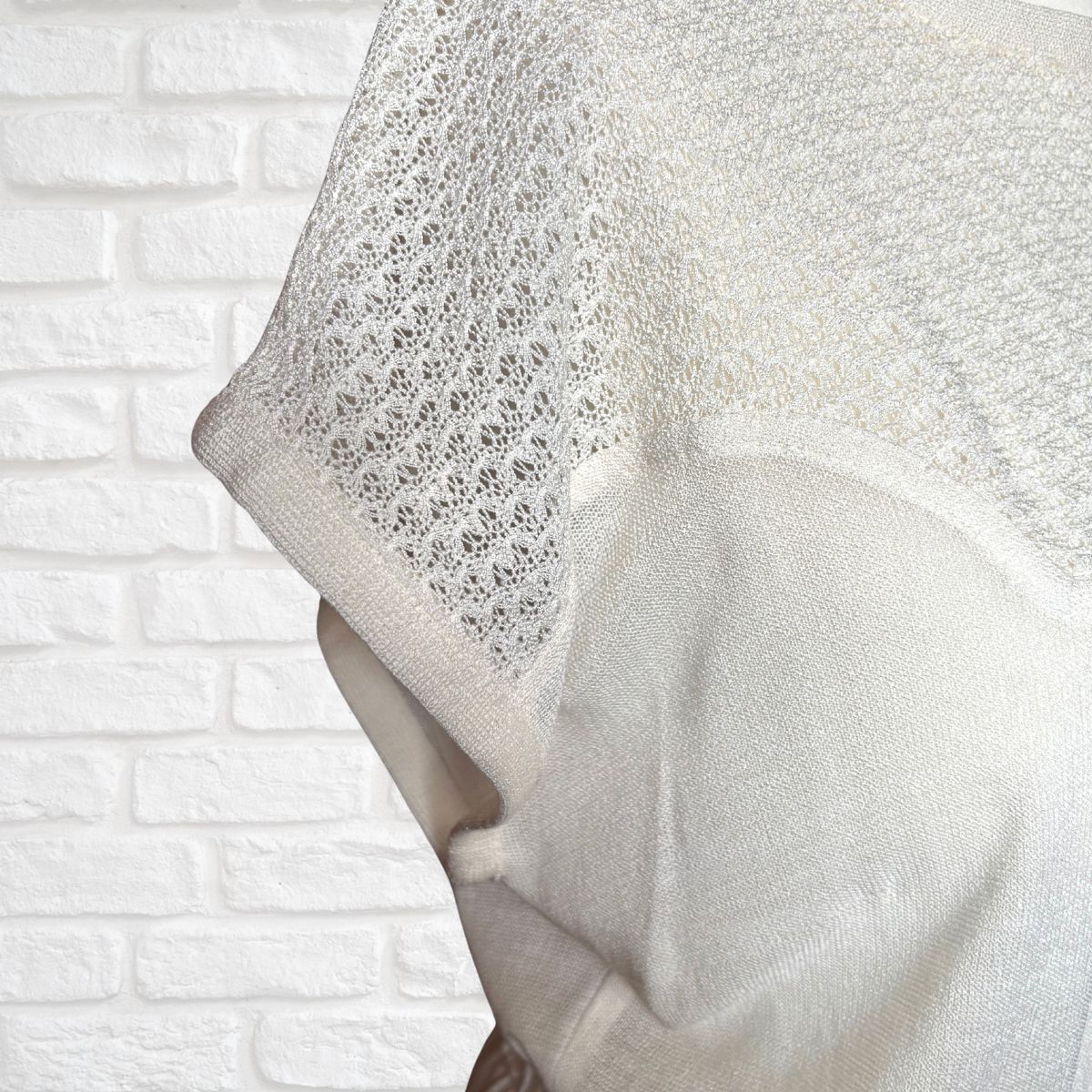 Close-up of a textured white knit dress against a white brick wall background