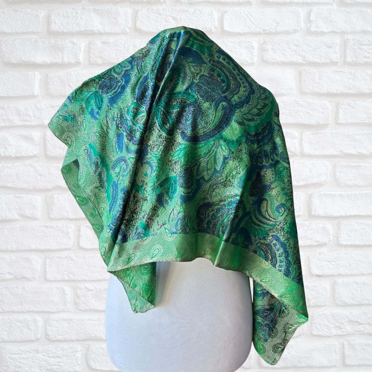 Green patterned fabric draped over a mannequin against a white brick wall.