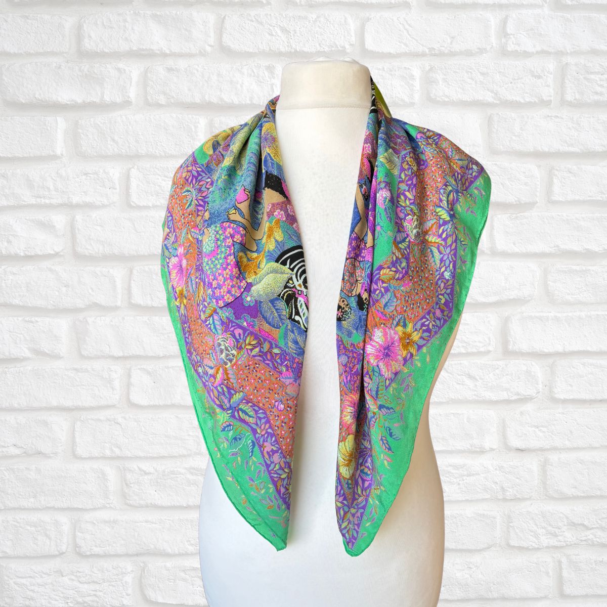 Colorful floral and patterned scarf on a mannequin against a white brick wall.