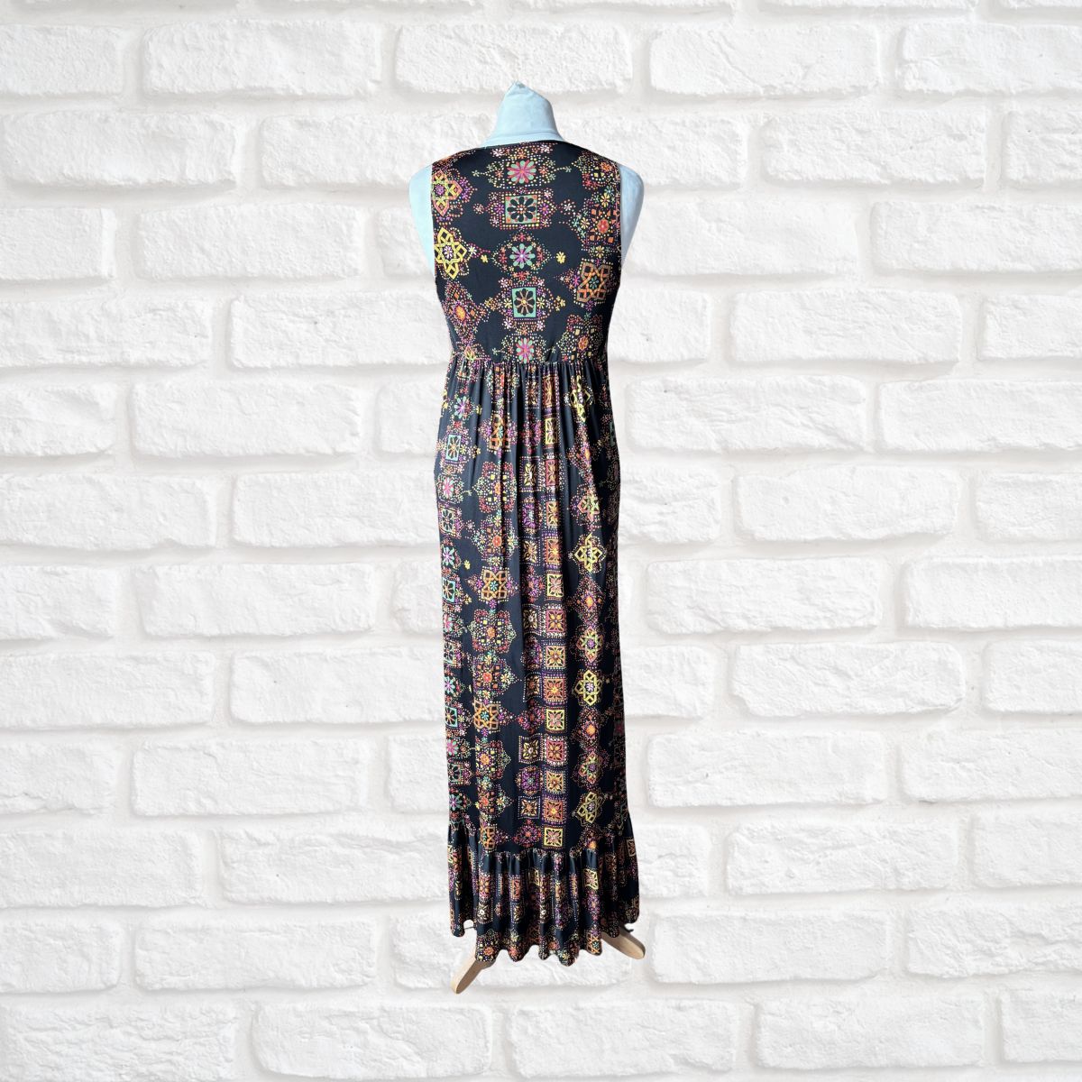 Sleeveless dress with a colorful pattern on a mannequin against a white brick wall.