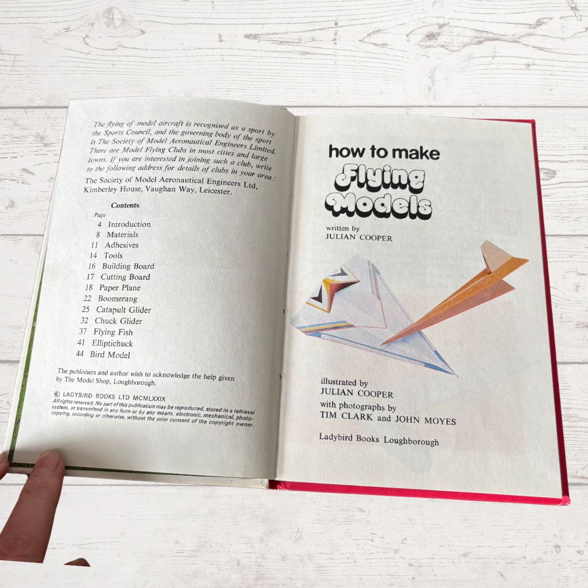 Open book titled 'How to Make Flying Models' with illustrations on a wooden surface