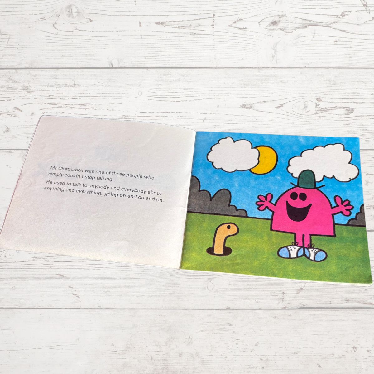 Open book with a colorful illustration of a pink character on a grassy area with a blue sky.