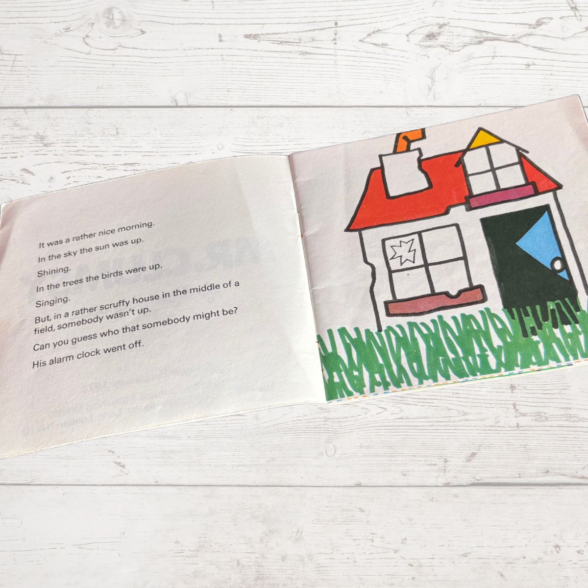 Open book with a colorful illustration of a house on a white wooden surface