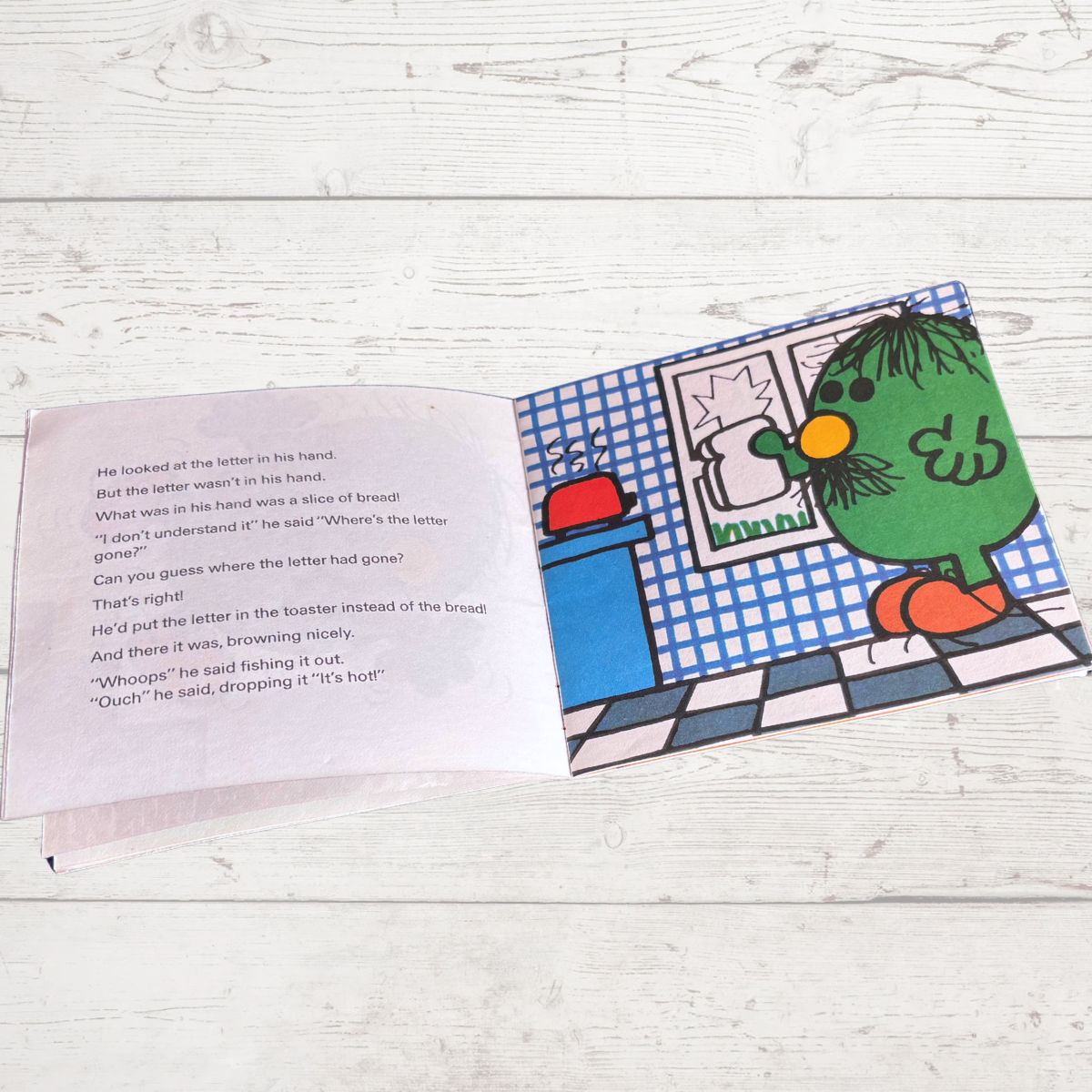 Open book with a green character on a wooden surface