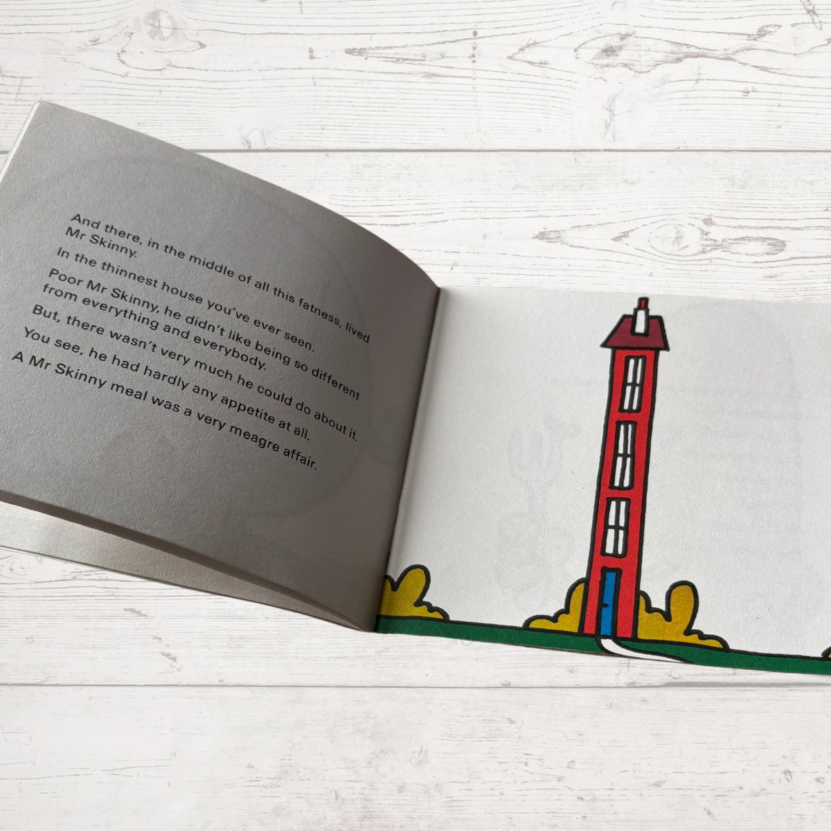 Open book with a drawing of a red lighthouse on a white wooden surface