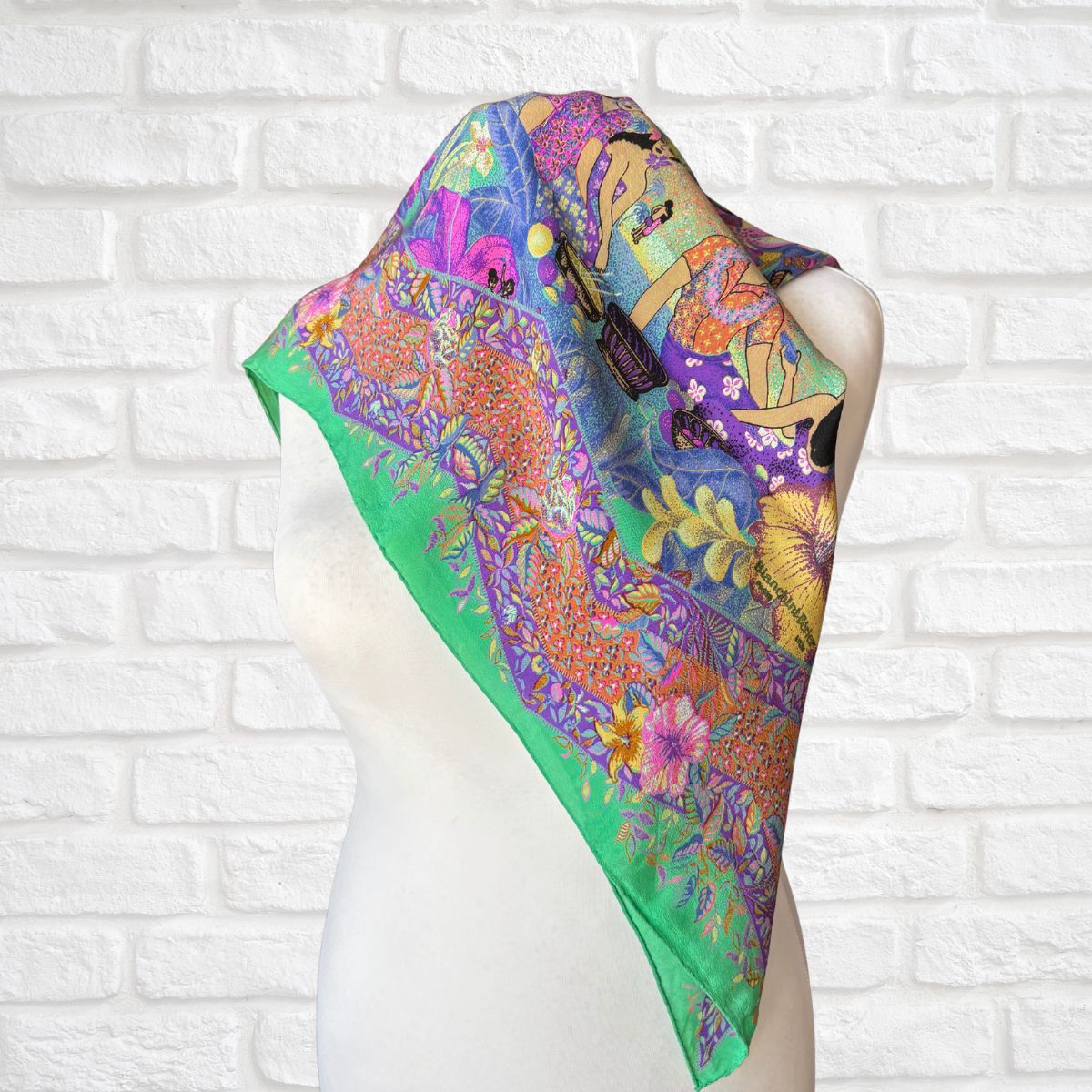 Colorful scarf with floral and abstract designs on a mannequin against a white brick wall.