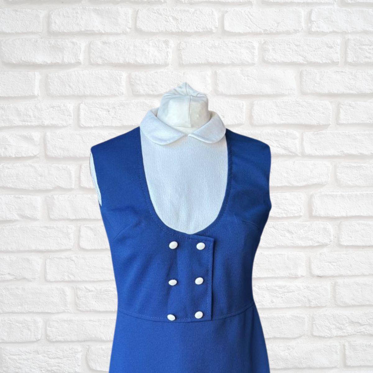 Blue dress with white collar on a mannequin against a white brick wall background