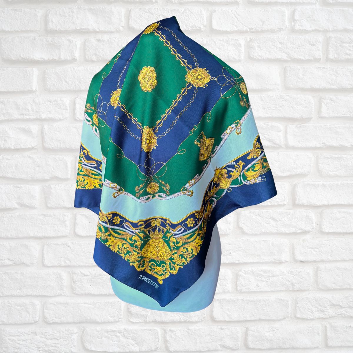 Colorful patterned scarf with gold accents on a white brick wall background