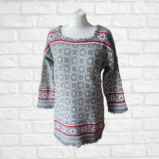 Gray, white and red Nordic patterned sweater on a mannequin against a white brick wall background