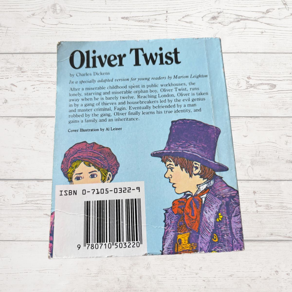 Back cover of 'Oliver Twist' book with illustrations and text on a light wooden surface