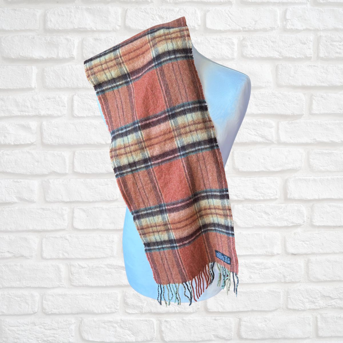 Plaid scarf on a mannequin against a white brick wall background