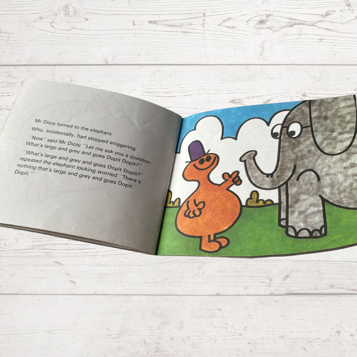 Open book with illustrations of an orange creature and an elephant on a wooden surface