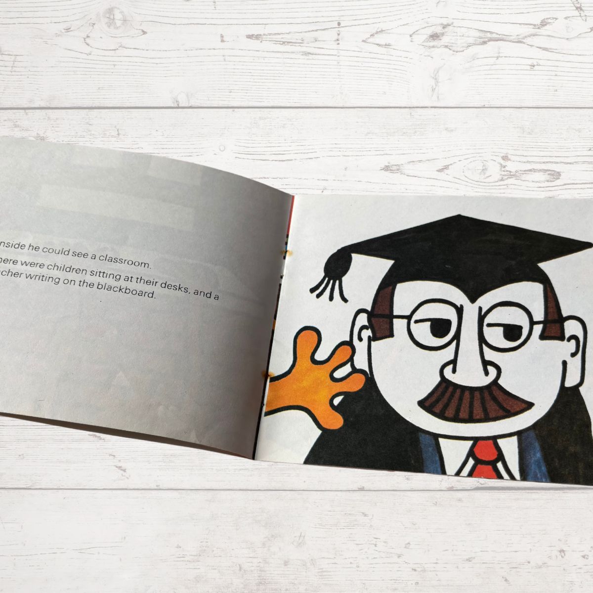 Open book with an illustration of a character in a graduation cap and gown on a wooden surface.