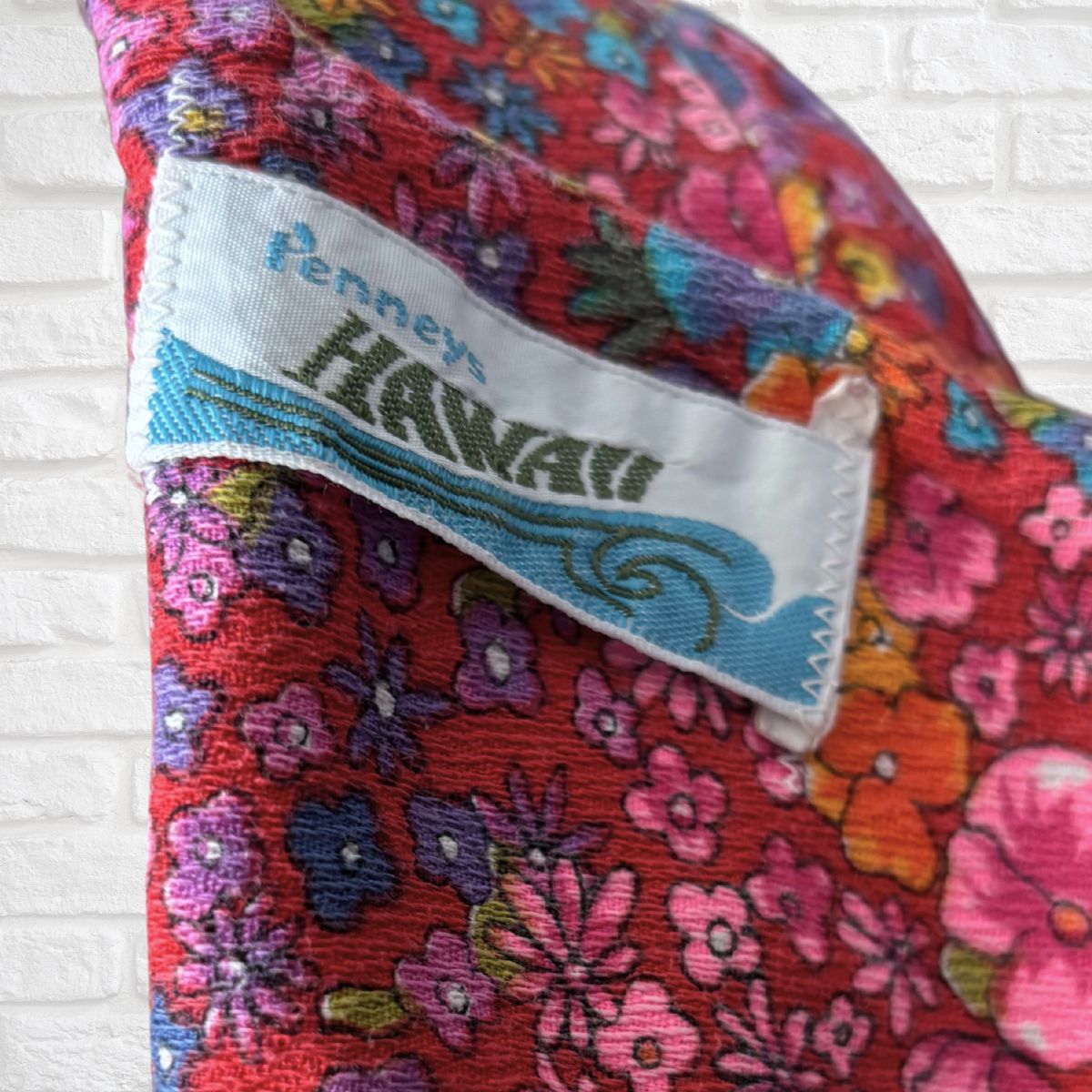 Floral-patterned fabric with a  ‘Pennys Hawaii' label on a white brick background
