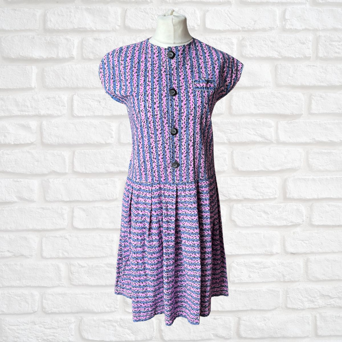 Purple and pink striped dress on a mannequin against a white brick wall background