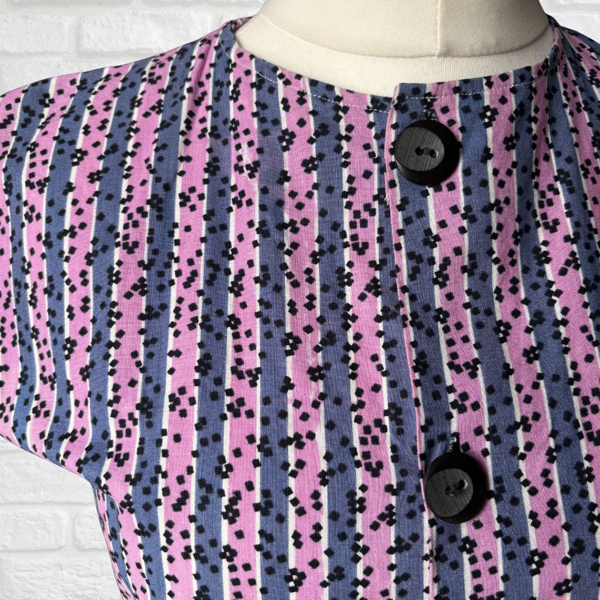 Mannequin wearing a dress  with a purple and pink striped pattern and black buttons.