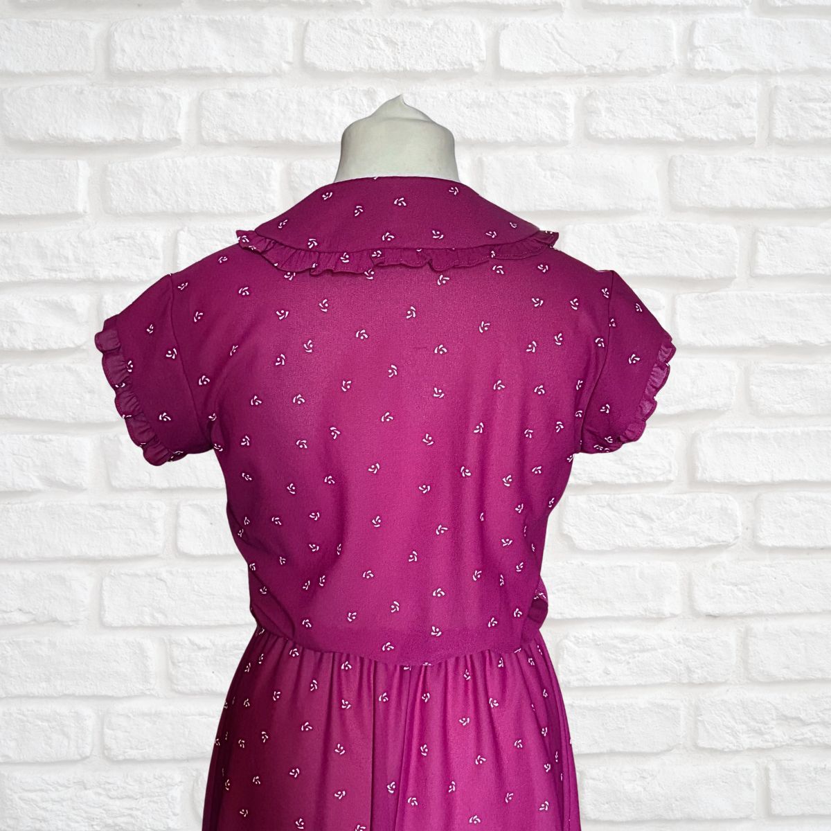 Purple dress with a pattern on a mannequin against a white brick wall background