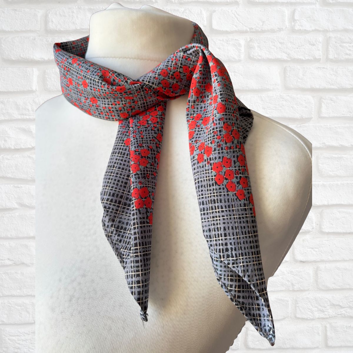 Scarf with red poppy and black pattern draped over a mannequin against a white brick wall.
