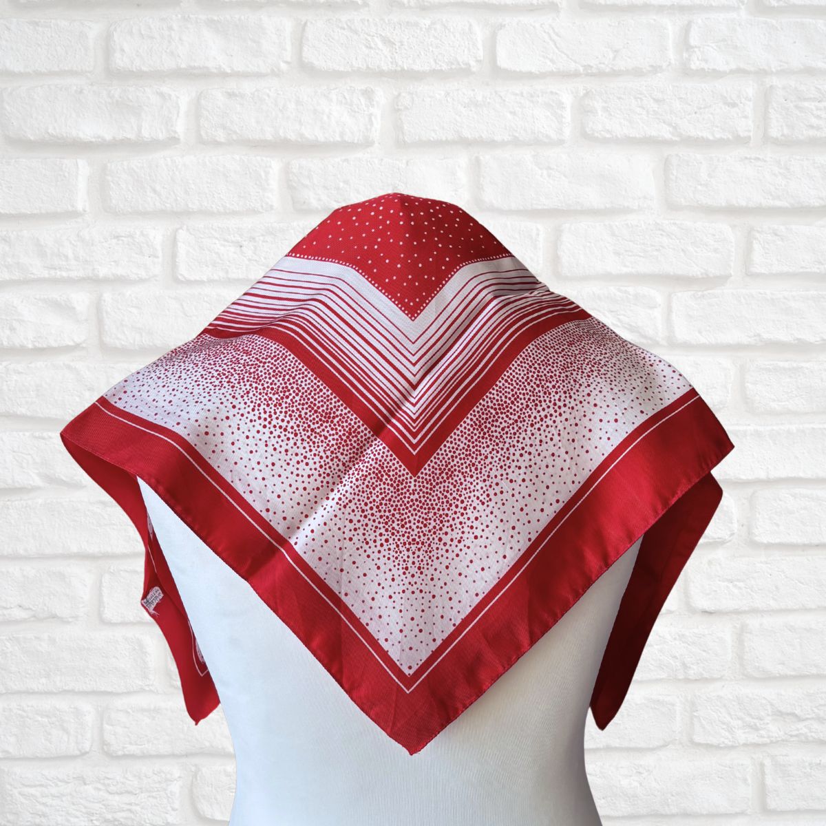 Red and white patterned scarf on a mannequin against a white brick wall background