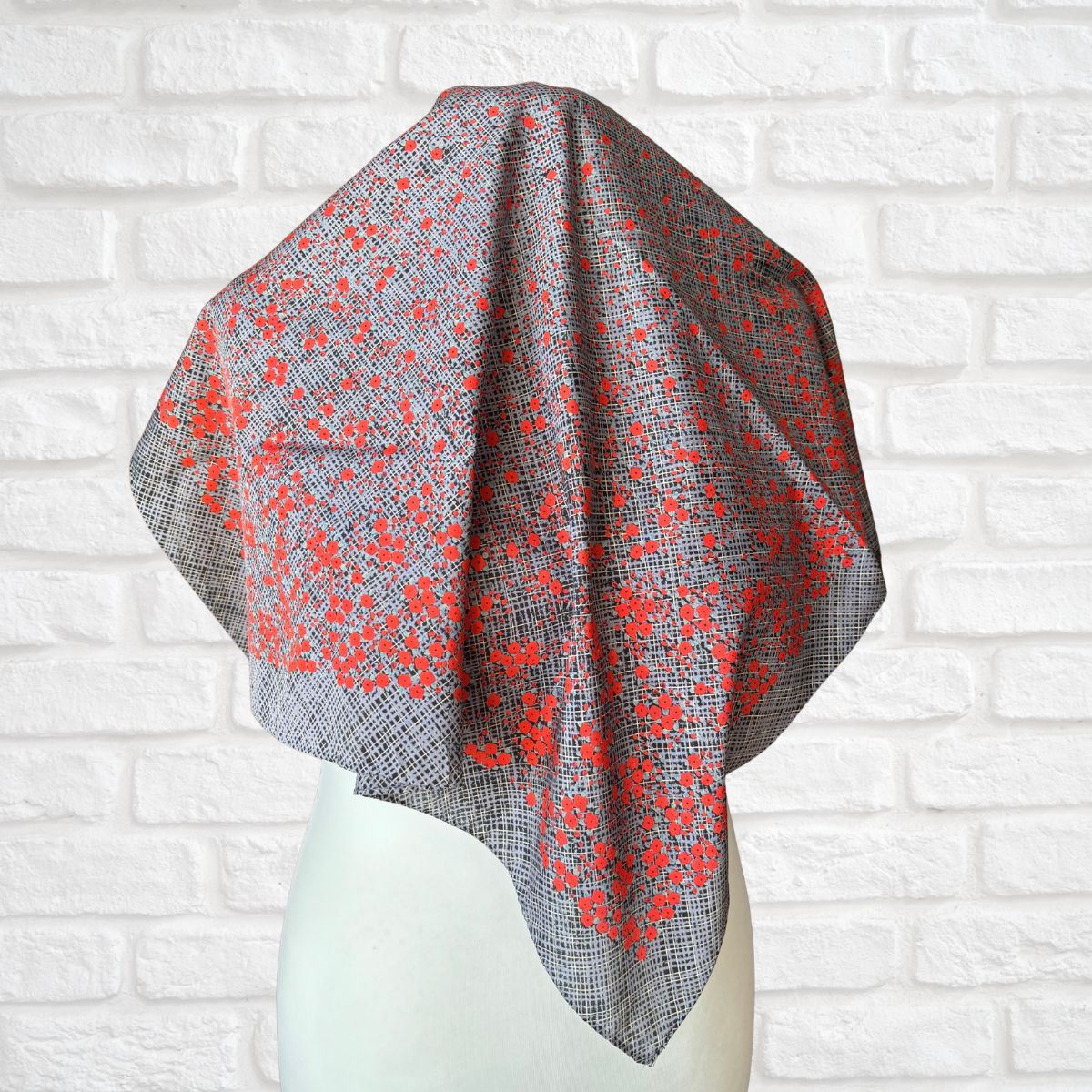 Gray and red patterned scarf on a mannequin against a white brick wall background