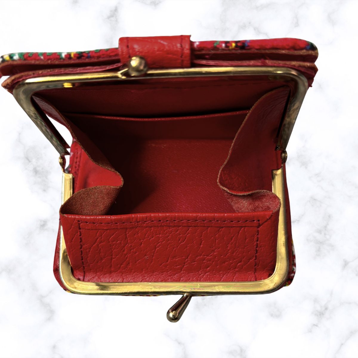Red leather coin purse with gold frame on a white marble background