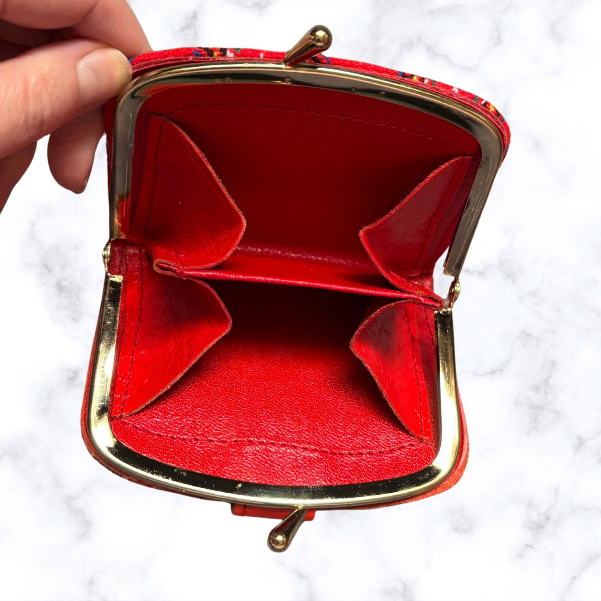 Red purse with gold frame held open by a hand on a white background