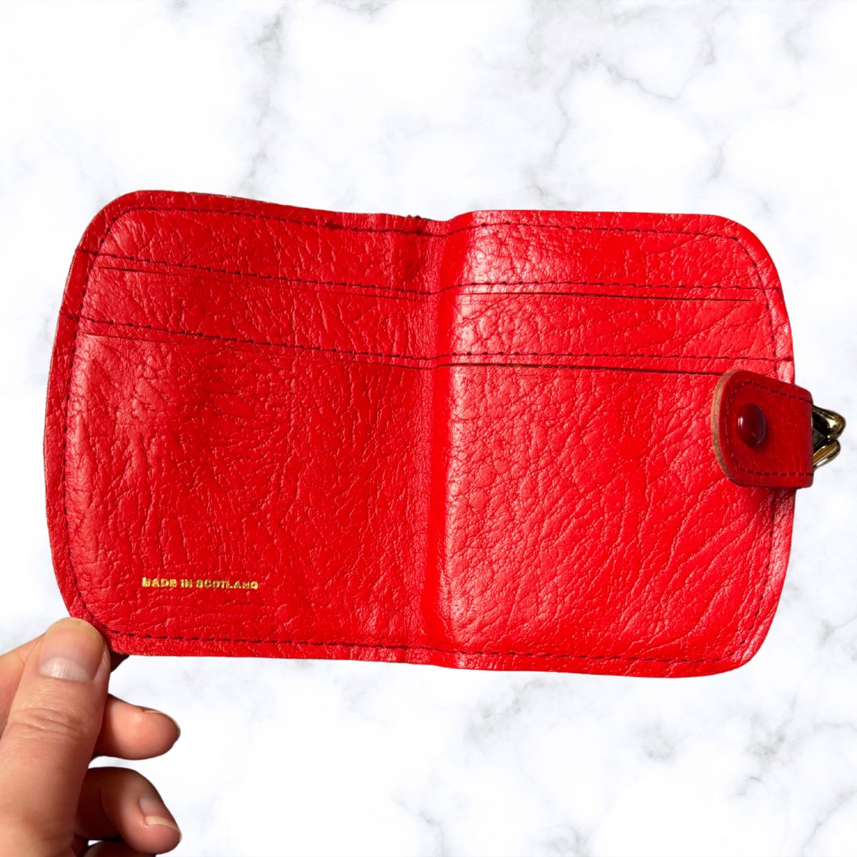 Red leather wallet held by a hand on a white background