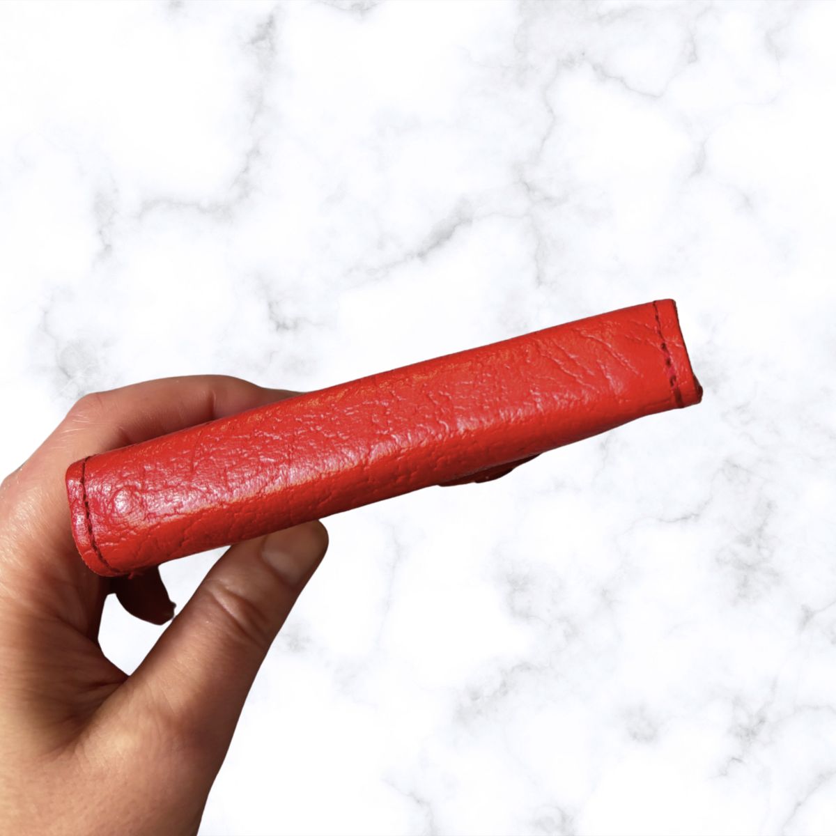 Red leather object held by a hand against a white marble background
