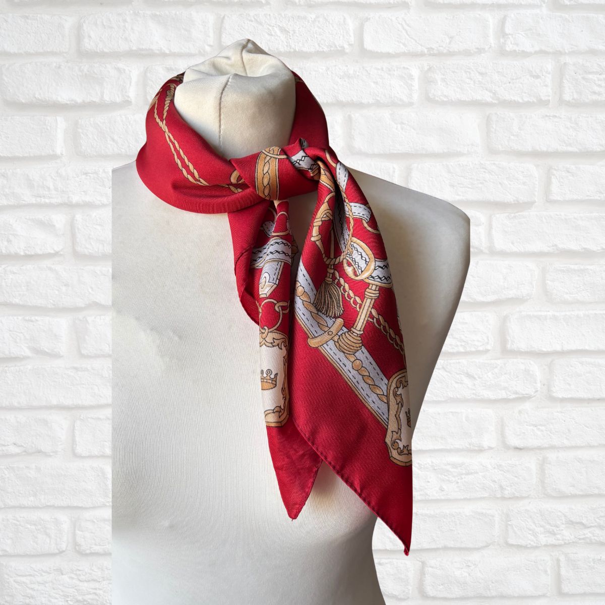 Red scarf with gold and white patterns on a mannequin against a white brick wall.