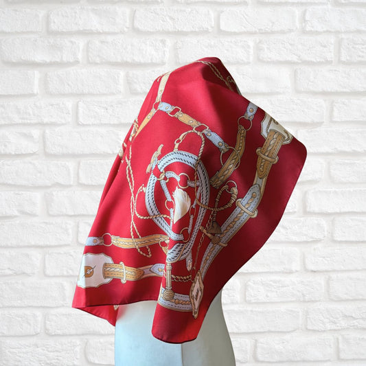 Red scarf with white and gold patterns on a mannequin against a white brick wall.