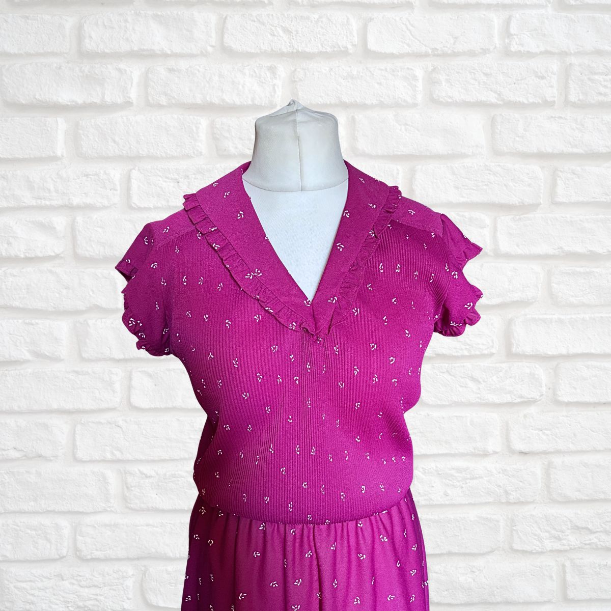 Pink dress with ruffled collar on a mannequin against a white brick wall background