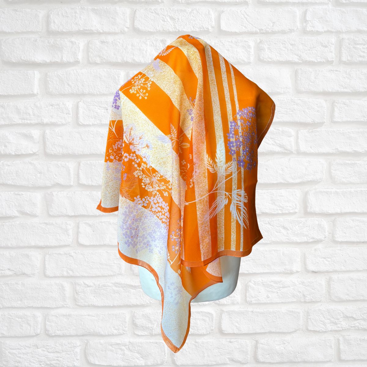 Orange and white floral patterned scarf on a mannequin against a white brick wall background