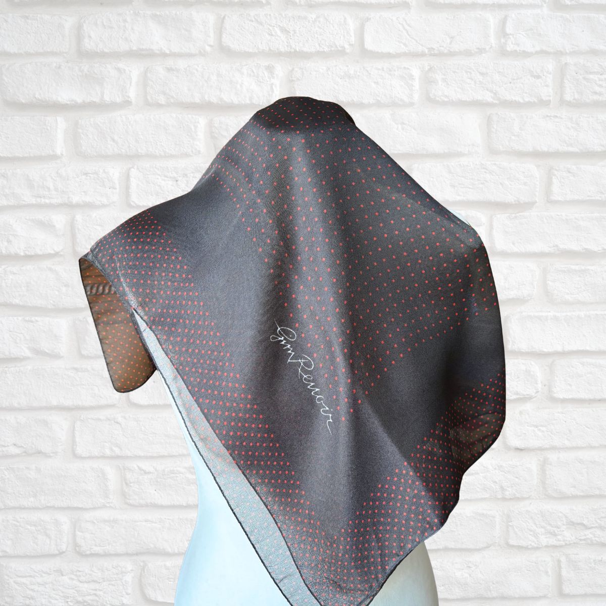 Black and red patterned scarf on a mannequin against a white brick wall.