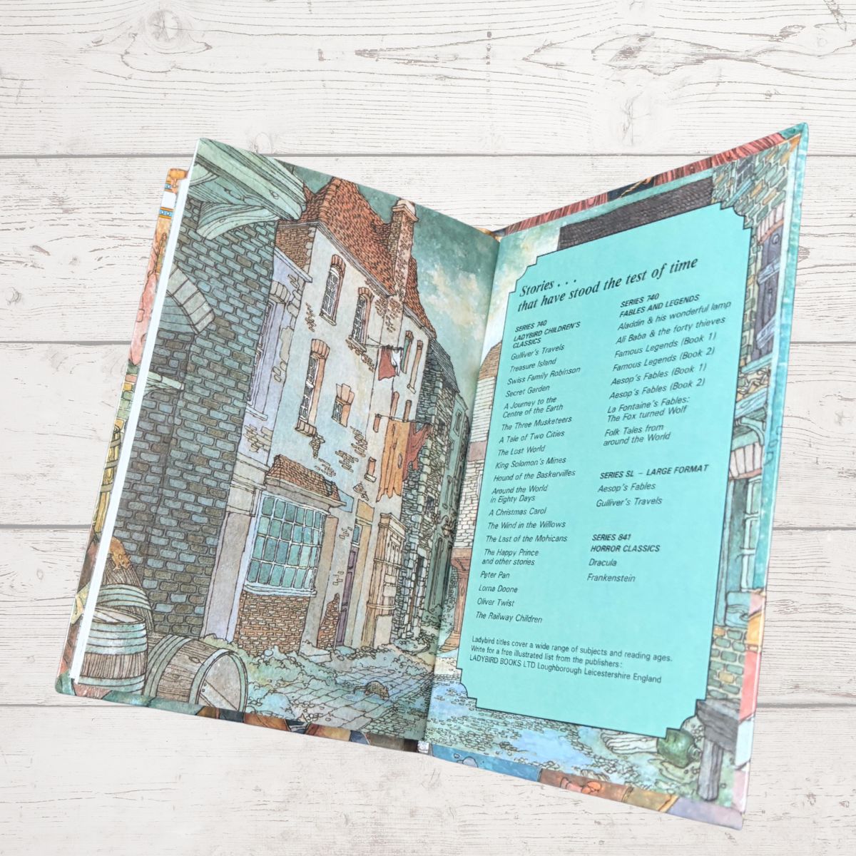 Open book with illustrated cityscape on one side and text on the other, on a wooden surface.