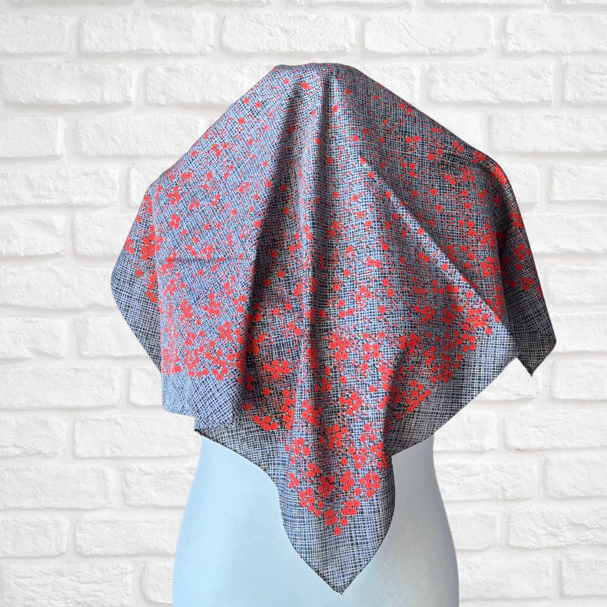 Gray and red patterned shawl draped over a mannequin against a white brick wall.