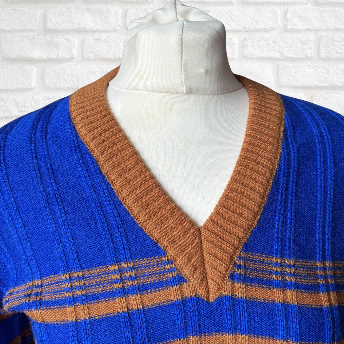 Blue and brown striped sweater on a mannequin against a white brick wall.