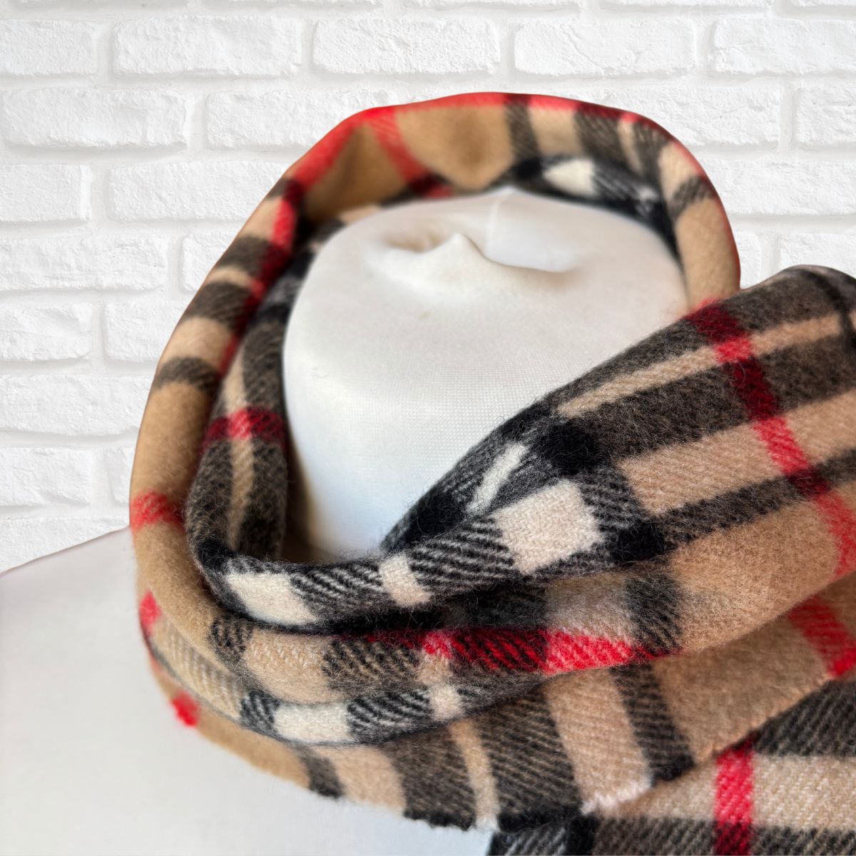 Plaid scarf draped over a mannequin head against a white brick wall background