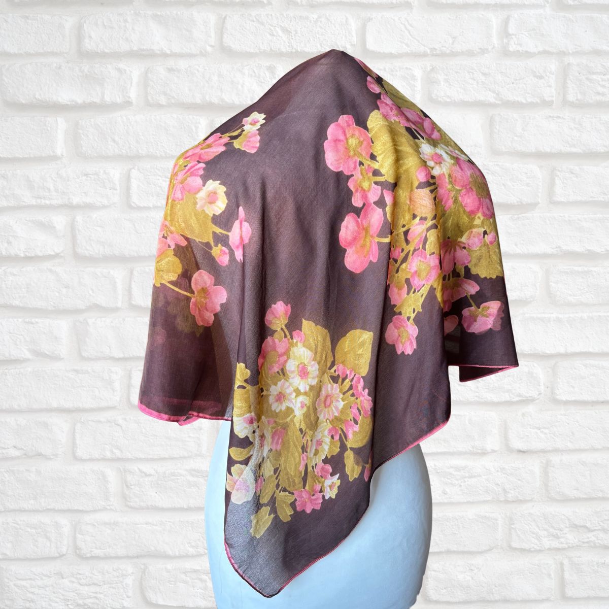 Floral patterned scarf on a mannequin against a white brick wall background