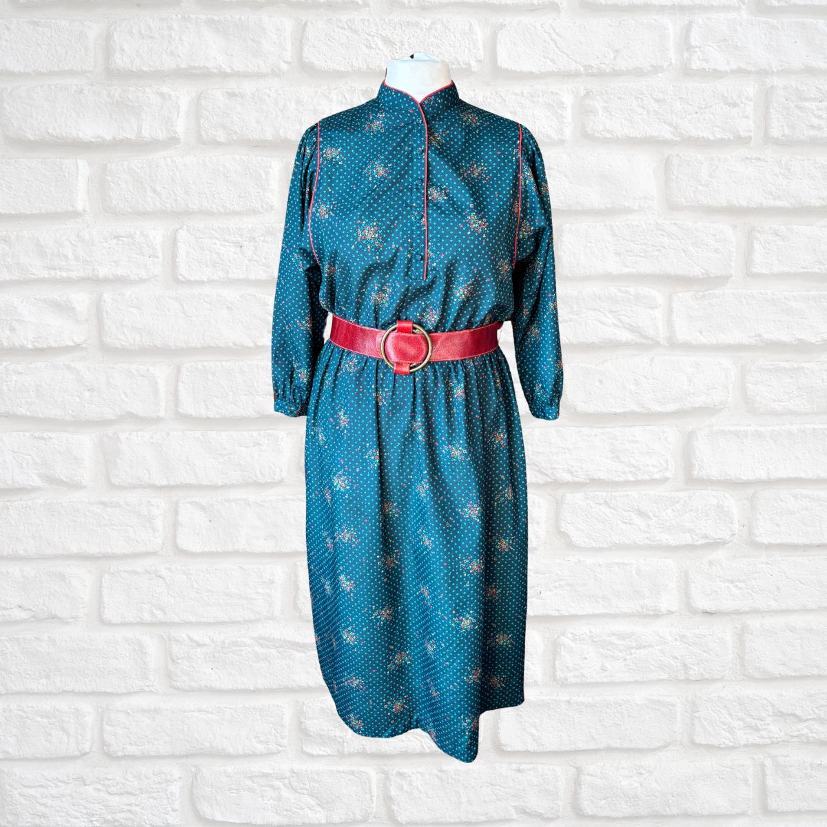 Blue dress with a red belt on a mannequin against a white brick wall background