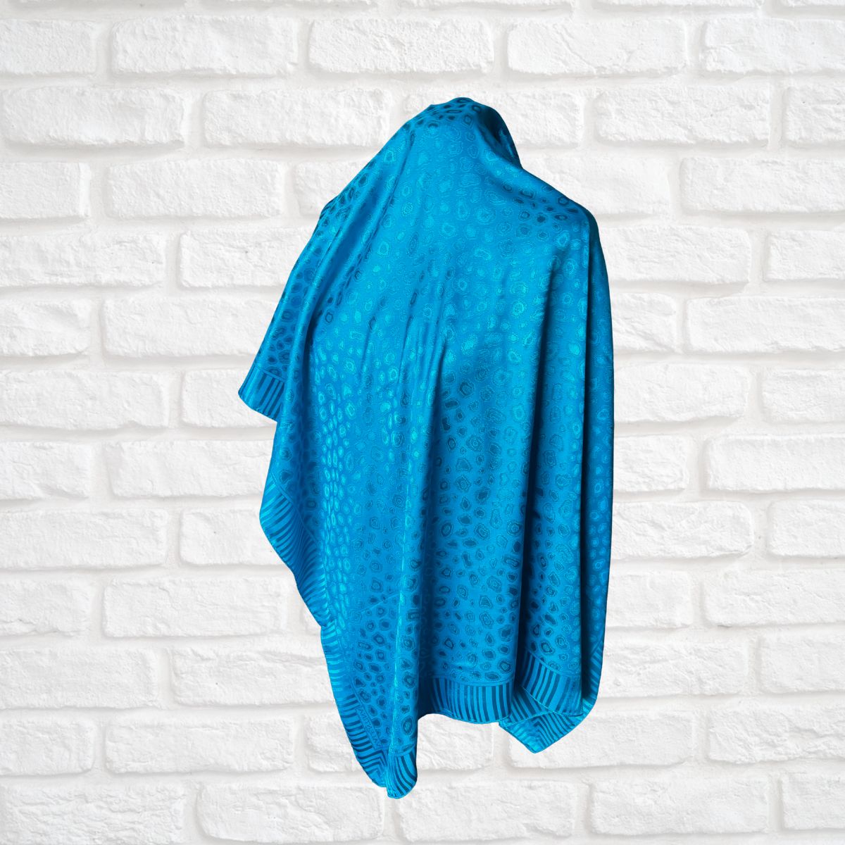 Blue scarf  hanging against a white brick wall