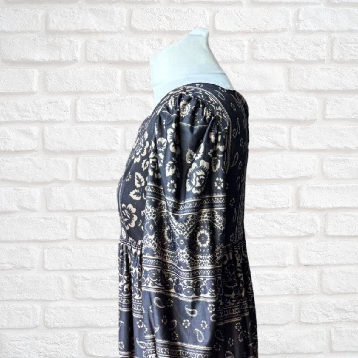 Black patterned dress on a mannequin against a white brick wall background