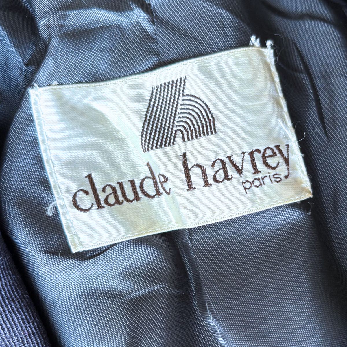 Clothing label with 'claude havrey paris' on a dark fabric background