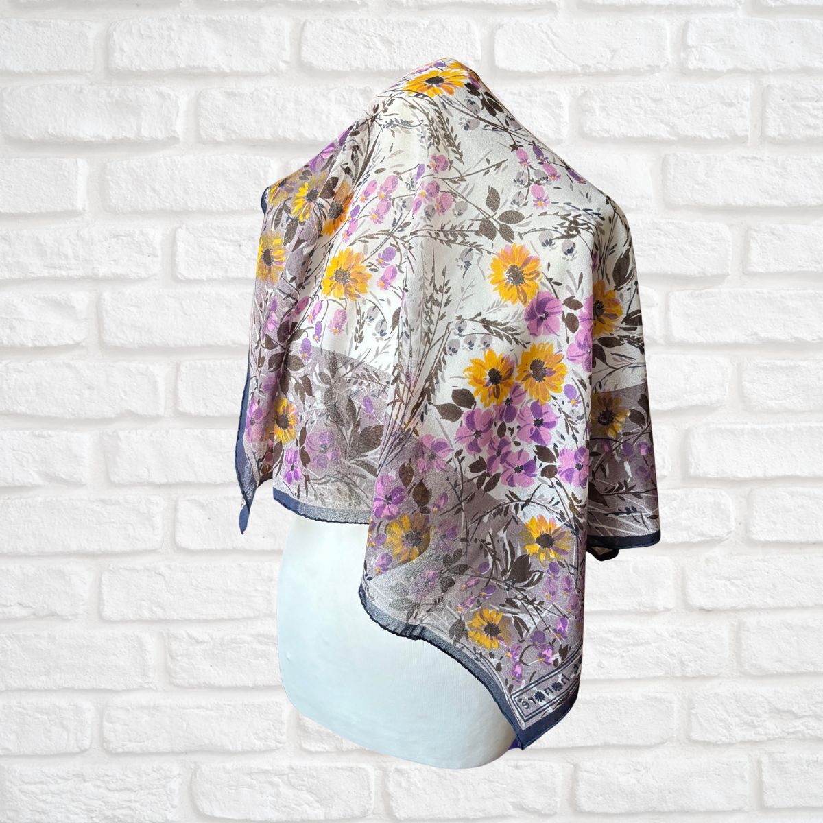 Floral patterned scarf on a mannequin against a white brick wall background