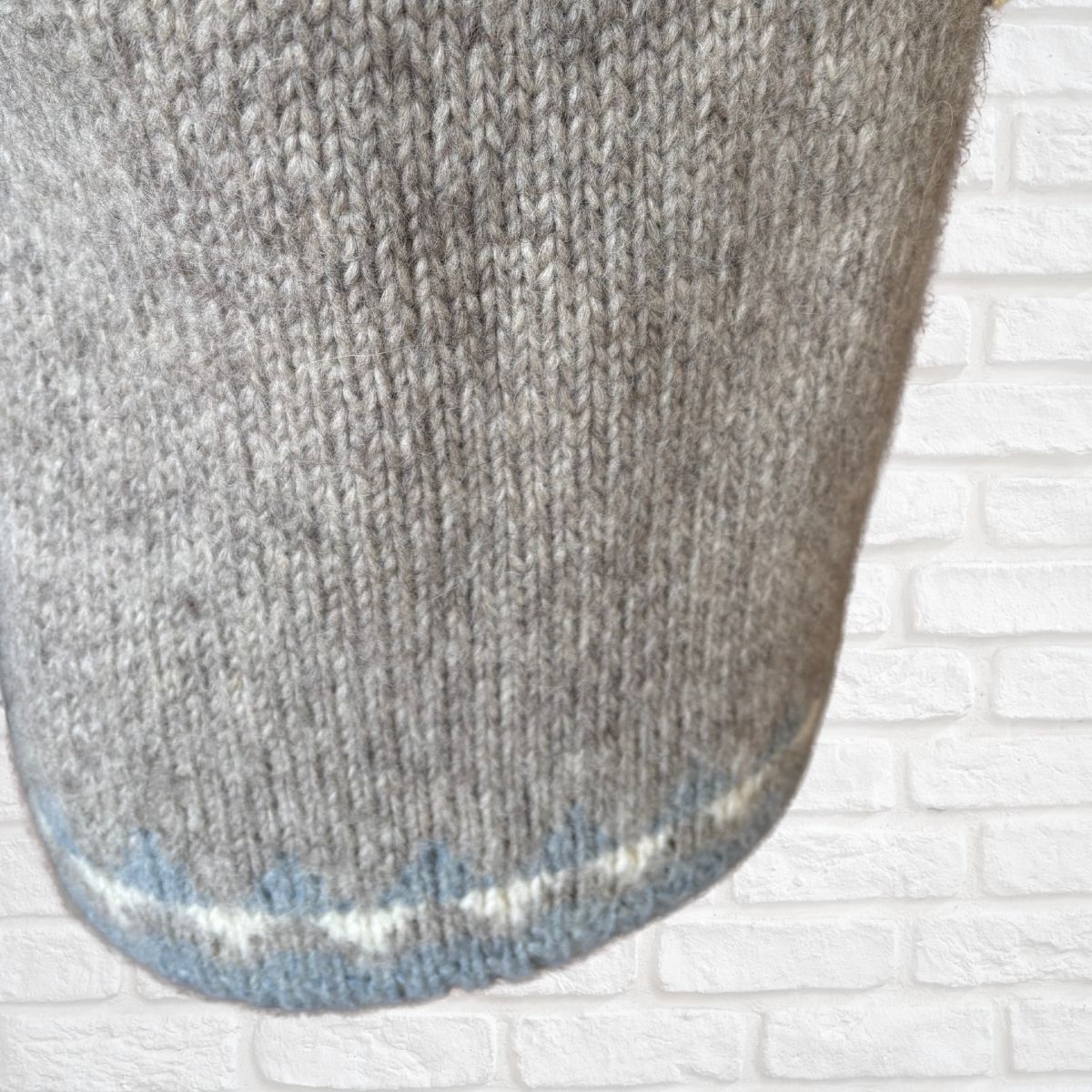 Close-up of a gray knitted sock on a white brick background