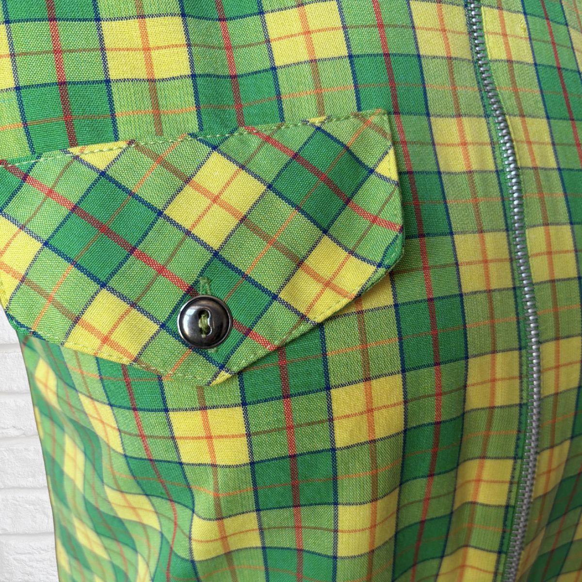 Close-up of a green and yellow plaid fabric with a button and zipper.