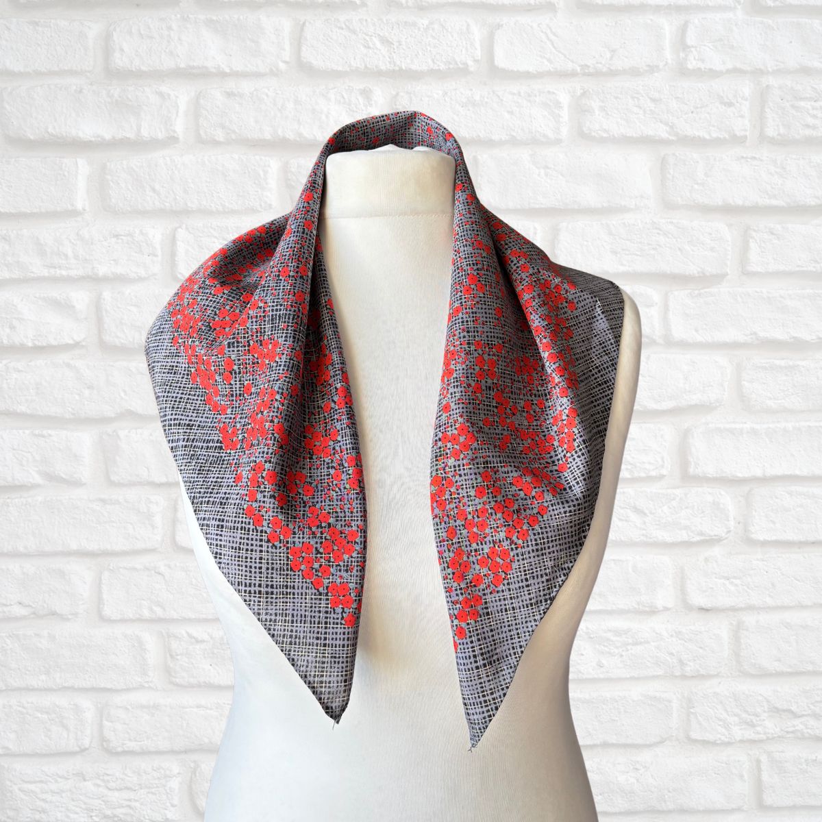 Scarf with red floral pattern draped over a mannequin against a white brick wall.