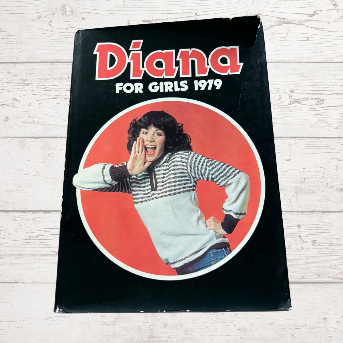 Book cover with a girl shouting, titled 'Diana for Girls 1979' on a wooden surface.