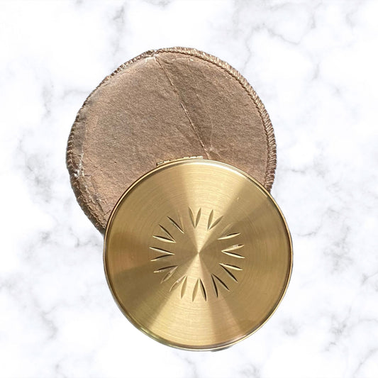 A gold tone convertible powder compact with a diamond cut sunburst design on the front. The compact is opened to show the inner mirror, and it is accompanied by a beige fabric pouch.